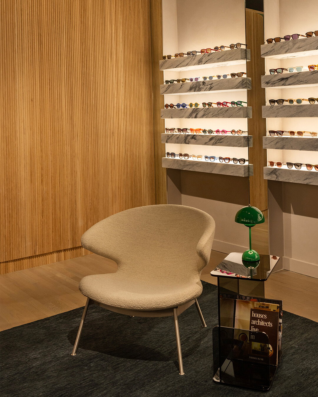 Image of the New York store with a focus on a beige chair and glass table. Shelves of glasses in the background.